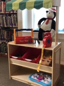 Photo is of the library's new marketplace learning center, which features a toy tool box, measuring tape, and other toys. The Cat in the Hat sits behind it. 